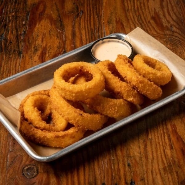 Golden-brown onion rings and a small cup of dipping sauce on a metal tray with parchment paper.