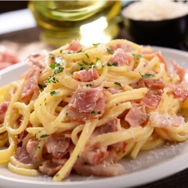 Creamy spaghetti carbonara with ham, parmesan, and parsley on a white plate.