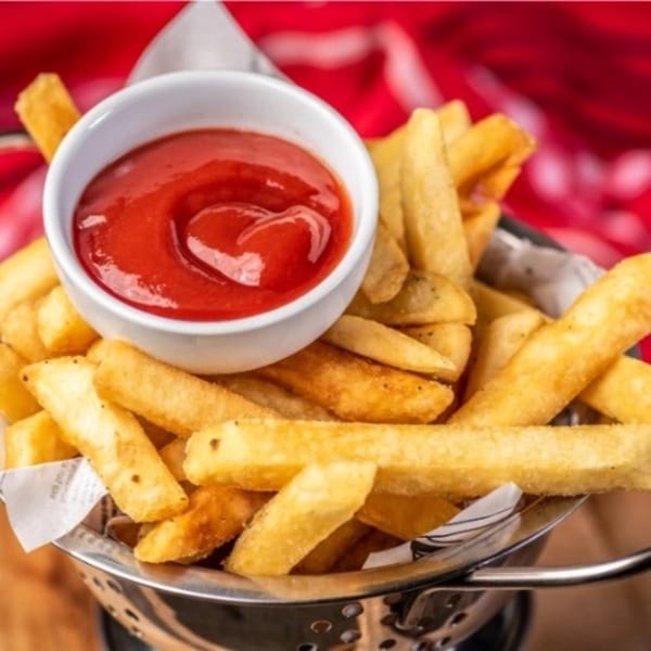 Golden french fries in a metal basket with a small white bowl of ketchup.