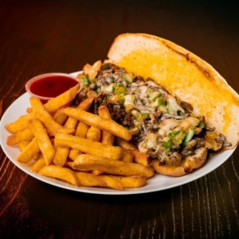 Deens Cheesesteak and Pizza's cheesesteak sandwich with fries and ketchup on a white plate.
