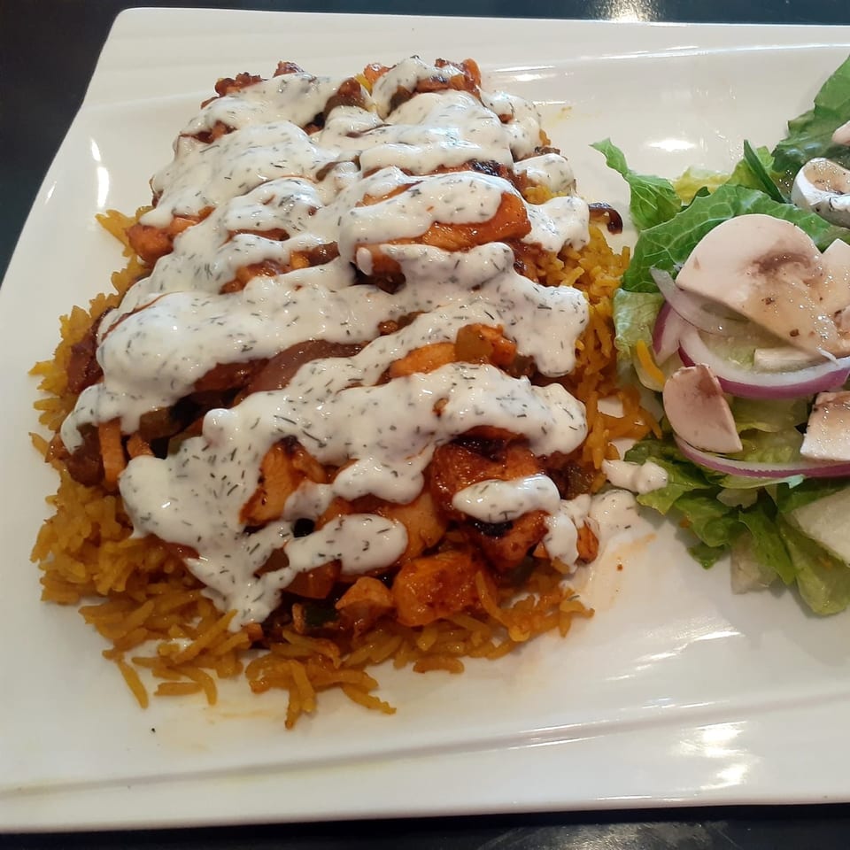 Chicken and rice platter with creamy white sauce and a side salad with mushrooms and red onion.
