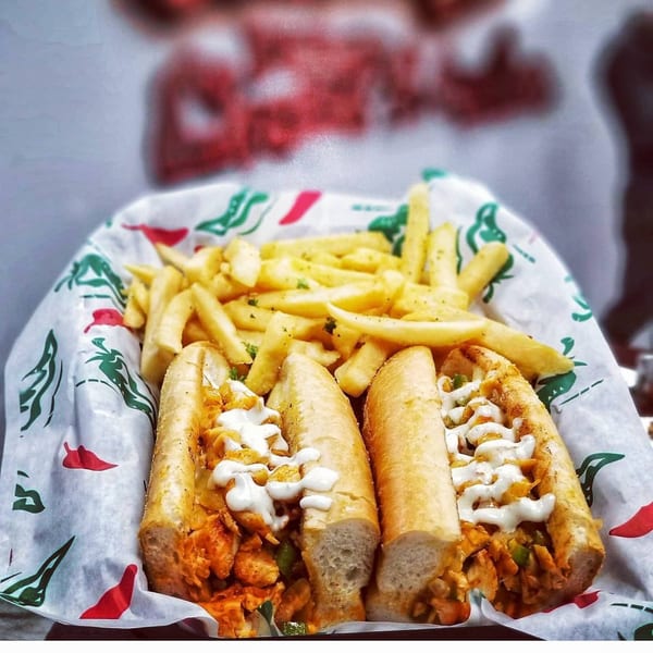 Two chicken cheesesteak sandwiches with fries, served in a paper-lined basket.