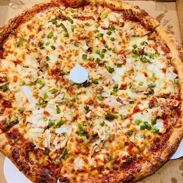 A whole Deens Cheesesteak & Pizza chicken pizza with green peppers and onions in a box.