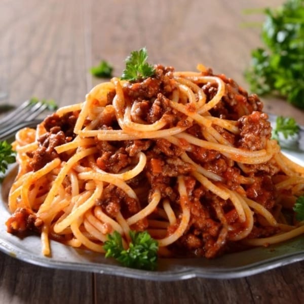 Spaghetti with meat sauce and parsley on a metal plate, on a rustic wooden table.