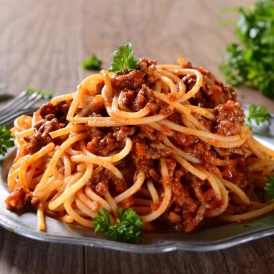 Spaghetti with meat sauce and parsley on a metal plate, on a rustic wooden table.